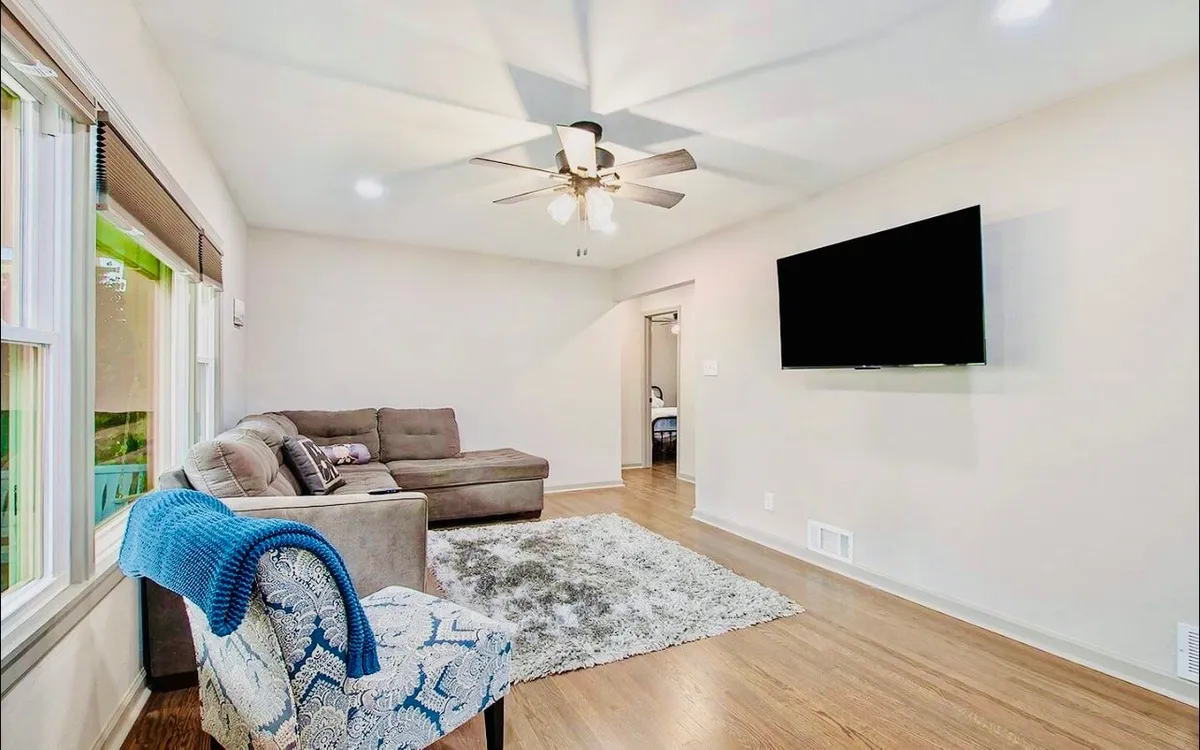 A cozy interior scene with a comfortable sofa, armchair, a large rug anchoring the space, and a TV set for movie nights or relaxing. The arrangement fosters intimacy and connection, suitable for both social and quiet moments.