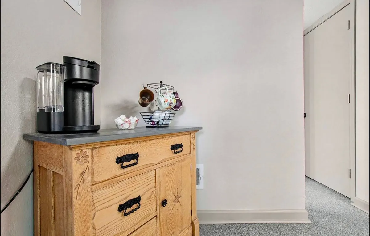 A charming corner of the cottage kitchen, highlighting a coffee maker, wooden cabinets, and a rack with mugs. It suggests leisurely mornings or intimate late-night conversations over a warm drink.