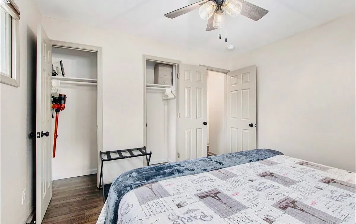 This image depicts a cozy bedroom with patterned bedding, a ceiling fan, and open closet doors. Sunlight gently filters into the room, evoking a sense of morning readiness and comfort. The visible open closet hints at a space for organizing clothing and gear.